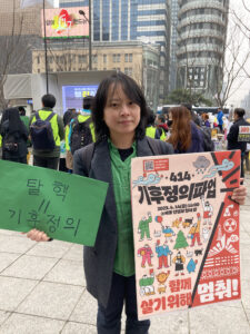 기후활동가 상현의 사진. 거리에서 두개의 피켓을 들고 있다. 오른손에는 탈핵=기후정의라고 적힌 피켓, 왼손에는 414기후정의파업, 함께 살기위해 멈춰!라고 적힌 피켓을 들었다.