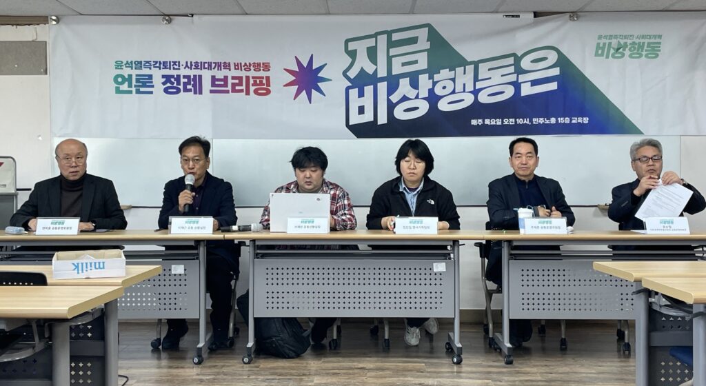 윤석열즉각퇴진 사회대개혁 비상행동 언론 정례 브리핑, 지금 비상행동은. 이라고 적힌 현수막 앞에 발언자 6명이 앉아있다. 왼쪽부터 안지중 공동운영위원장, 이재근·서채완 공동 상황실장, 정진임 행사기획팀장, 주제준 공동운영위원장, 윤순철 사회대개혁특위 공동위원장.