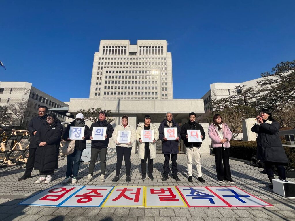 대법원 앞에서 고개를 숙인채 피켓을 들고 있는 사람들의 모습. '정의는죽었다'라는 문구가 한 글자씩 적힌 피켓을 들고 있고, 바닥에는 '엄중처벌촉구'라고 적힌 대형 피켓들이 놓여있다. 일부는 눈물을 흘리고 있는 모습.