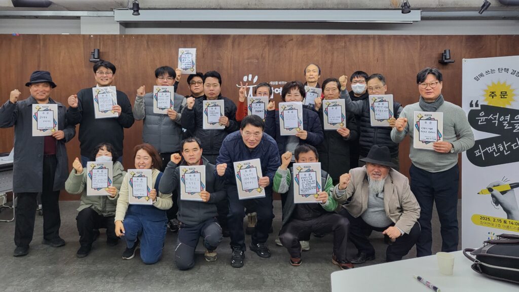 함께 쓰는 탄핵결정문 행사에 참여한 참가자들의 단체 사진. 각자가 쓴 주문 피켓을 들고 파이팅하는 듯 주먹을 치켜들고 있다.
