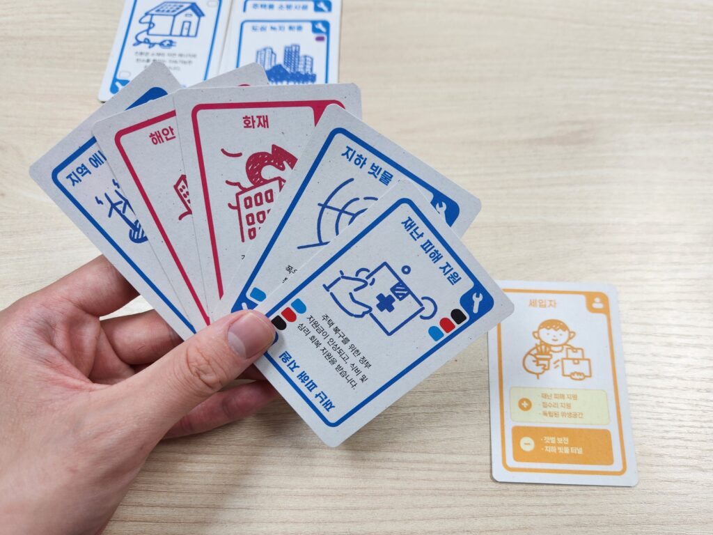 세입자 역할카드가 놓여있고, 세입자의 +대안 요소인 재난피해지원카드를 손에 들고 있다.