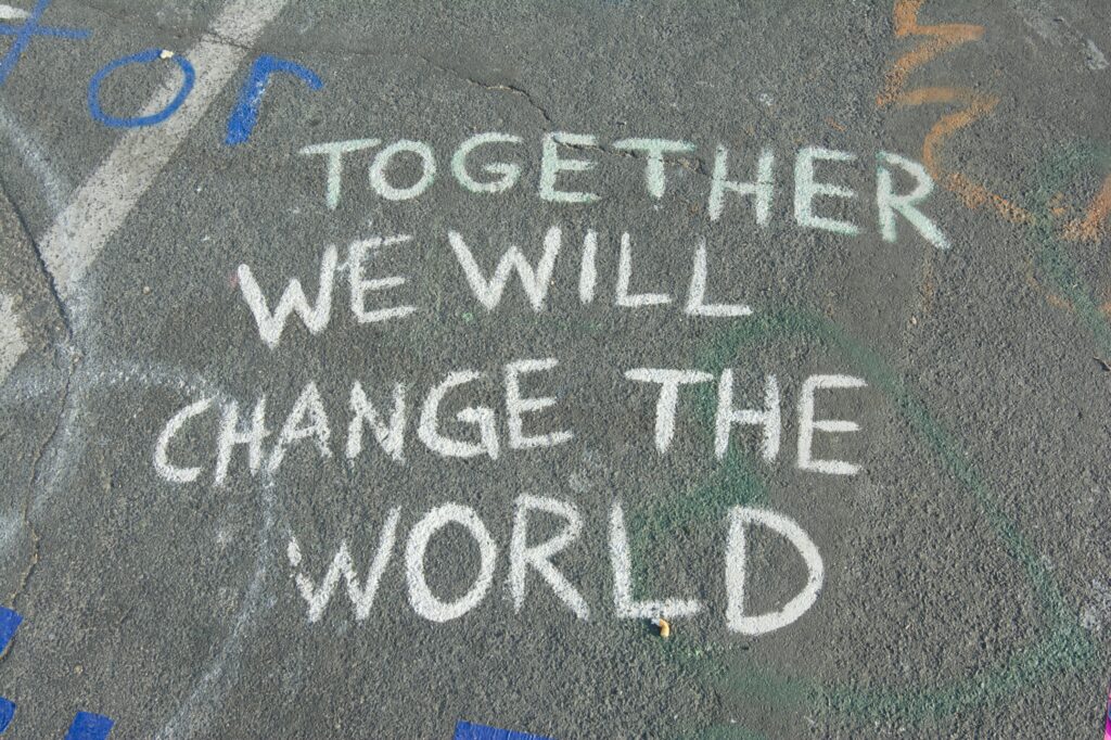 도로 위에 분필로 'TOGETHER WE WILL CHANGE THE WORLD'라고 적혀 있는 사진.