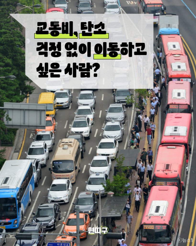 차들이 가득 늘어서있는 차도, 왼편으로는 승용차가 가득하고, 오른편 차선에는 광역버스가 줄지어 서있다. 중앙 버스정류장에는 사람들이 서있다. 화면 왼쪽에는 “교통비, 탄소 걱정 없이 이동하고 싶은 사람?”라는 문구가 강조되어 있다.