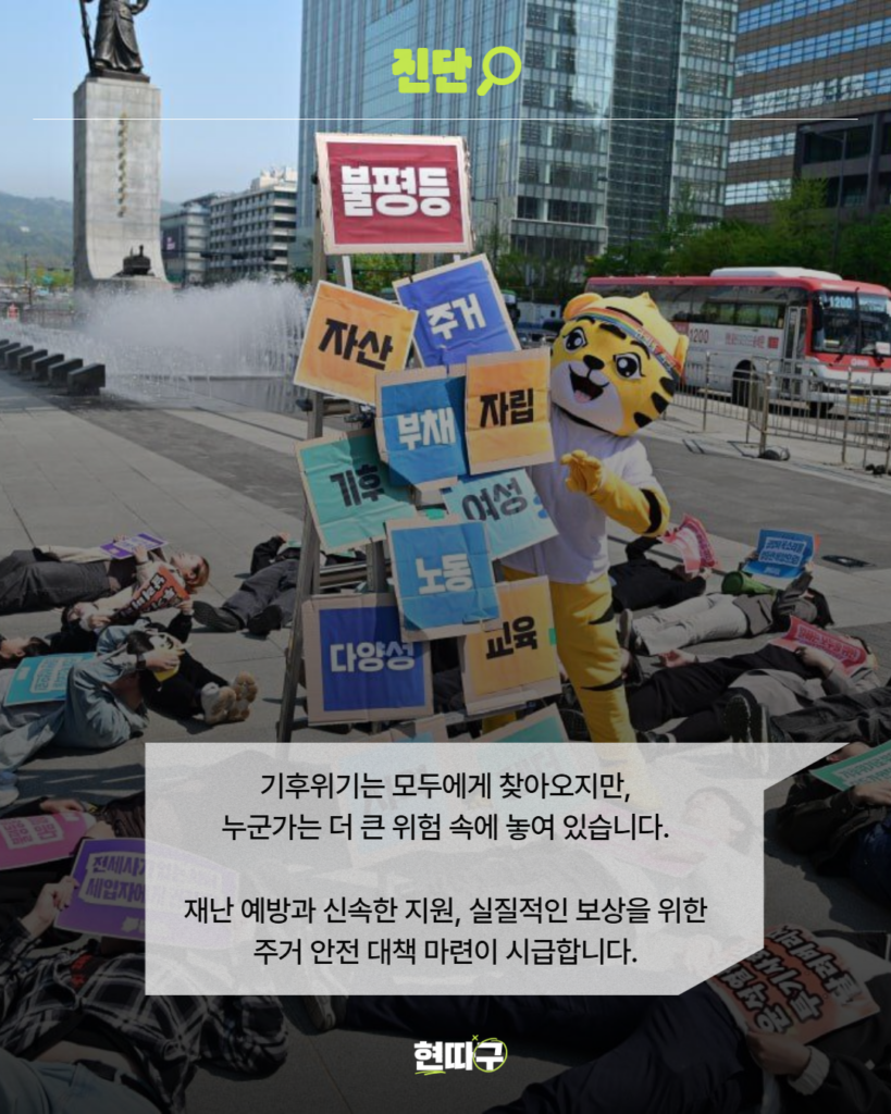 도심 광장에서 퍼포먼스를 하는 장면. 호랑이 캐릭터 탈을 쓴 사람이 ‘불평등’, ‘자산’, ‘부채’, ‘노동’ 등의 단어가 적힌 팻말들 앞에 서 있고, 주변에는 사람들이 바닥에 누워 있다. 기후위기는 모두에게 찾아오지만, 누군가는 더 큰 위험 속에 놓여 있습니다. 재난 예방과 신속한 지원, 실질적인 보상을 위한 주거 안전 대책 마련이 시급합니다.